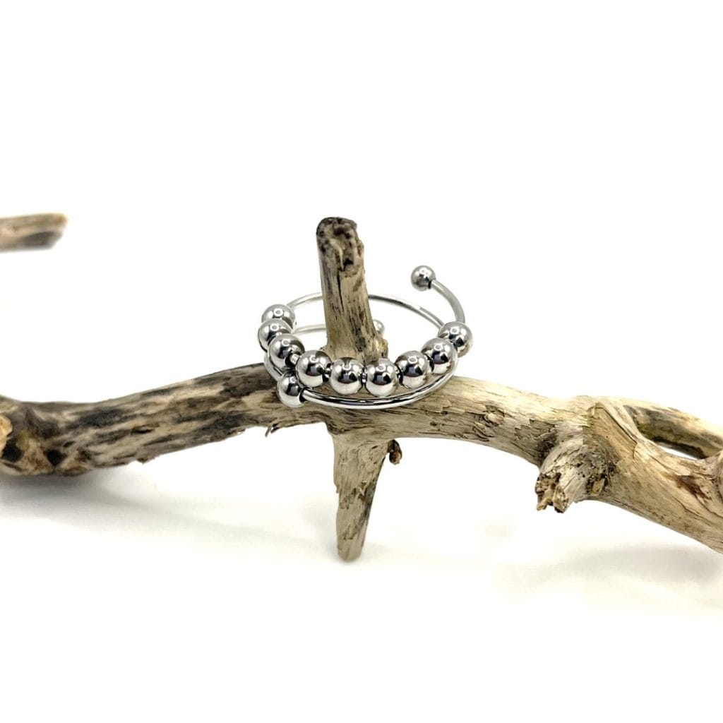 Meilleure bague anti-stress 2026 : comparatif et conseils pour bien choisir 2 Bague anti-stress Aurora argentée à plusieurs rangées de grosses billes, posée sur du bois flotté
