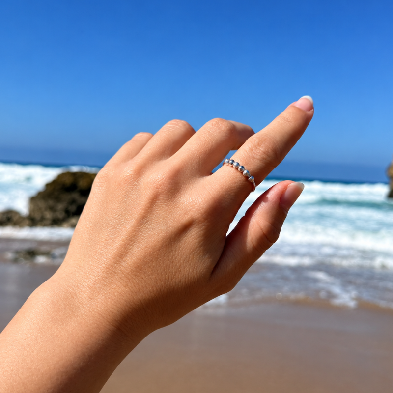 La bague anti-stress fonctionne-t-elle vraiment ? Ce qu’il faut savoir 2 Main portant une bague anti-stress argentée à billes face à la mer