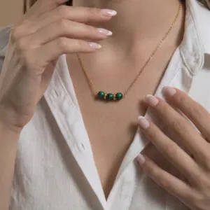 Collier doré en malachite Aïda porté sur une chemise blanche, trois pierres naturelles sur chaîne