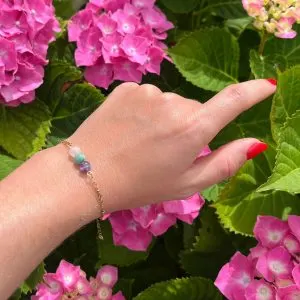 Bracelet chaîne Etnea Amour fin aux pierres colorées porté devant des hortensias roses